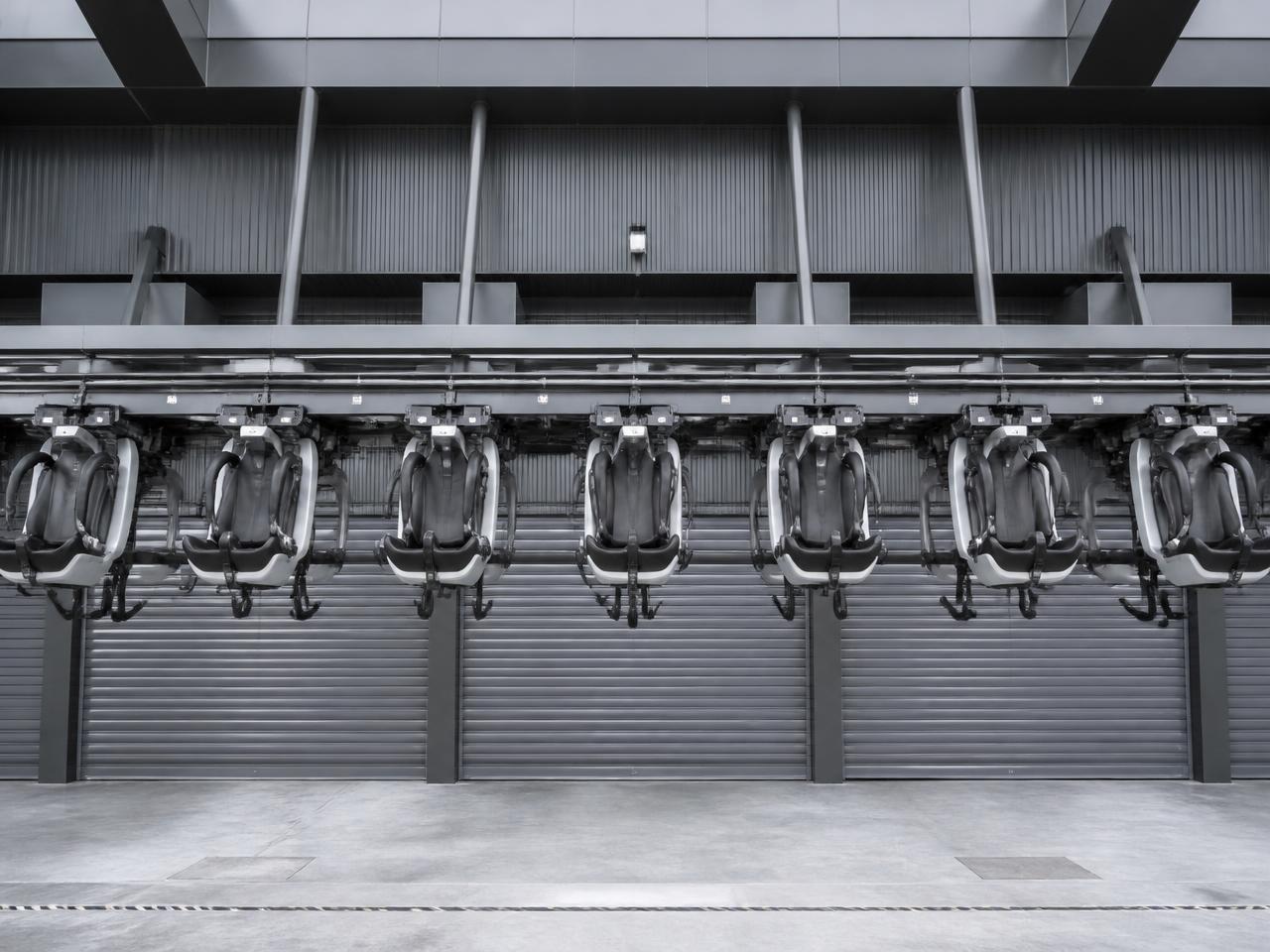 A row of suspended motion seats with dangling footrests and shoulder restraints, facing the closed garage doors of the theater